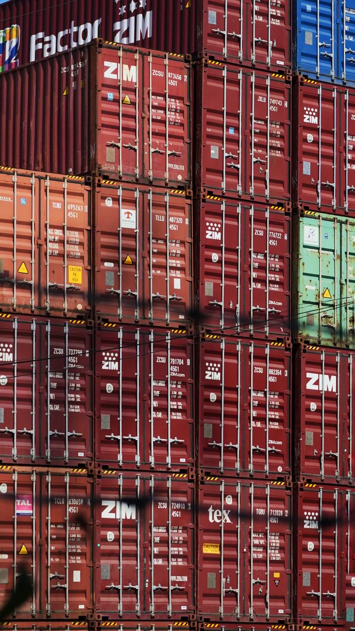 services-03 Vertical shot of colorful, stacked shipping containers at a bustling cargo port.