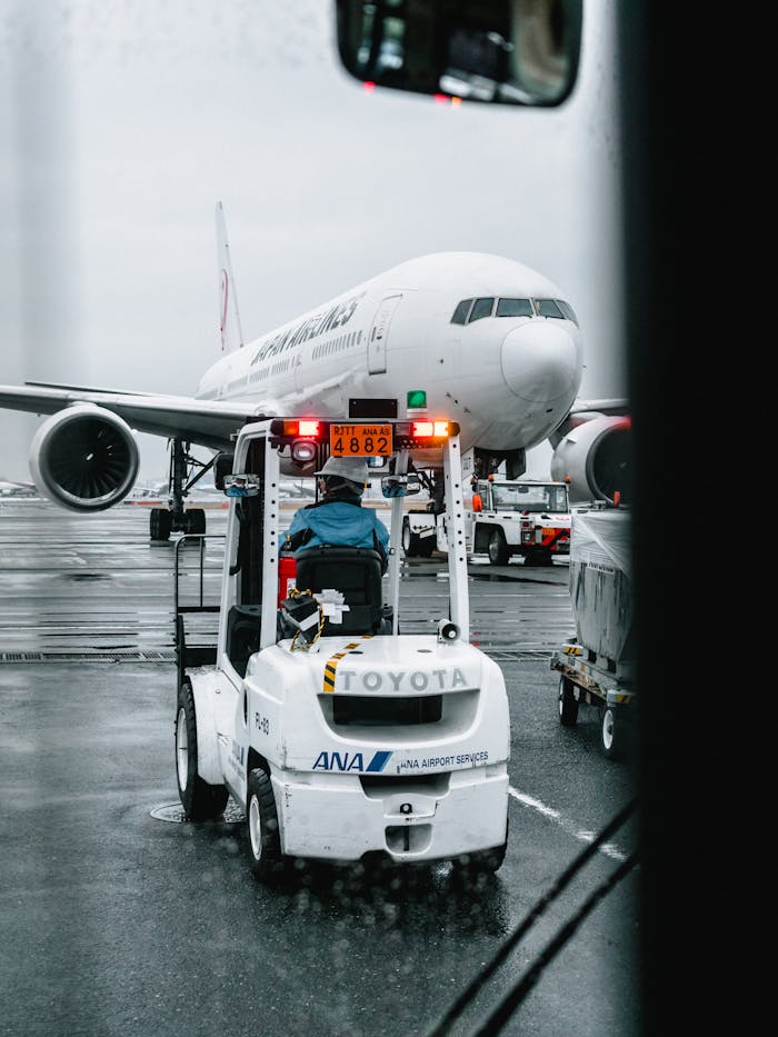 gallery-6 Airport ground crew operating a vehicle in front of a parked airliner on a rainy runway.