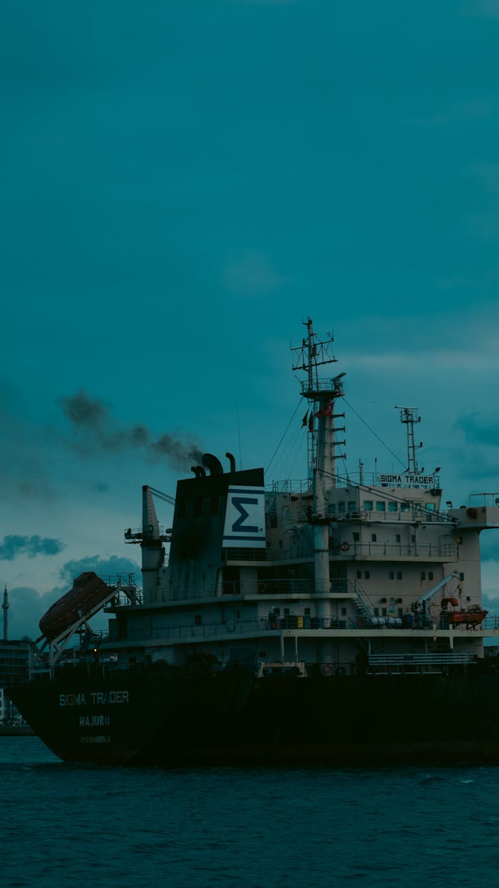 about-01 Majestic cargo ship emits smoke while sailing through calm waters at twilight, showcasing maritime industry.