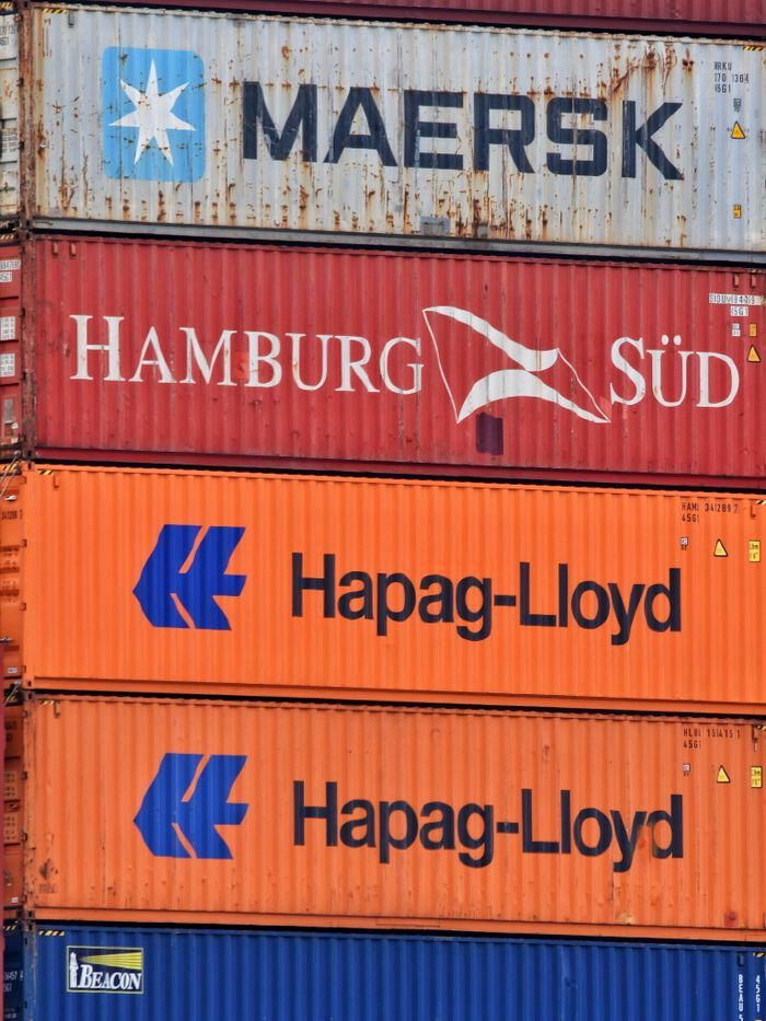 services-02 Close-up of stacked shipping containers featuring Maersk, Hamburg Süd, and Hapag-Lloyd logos.